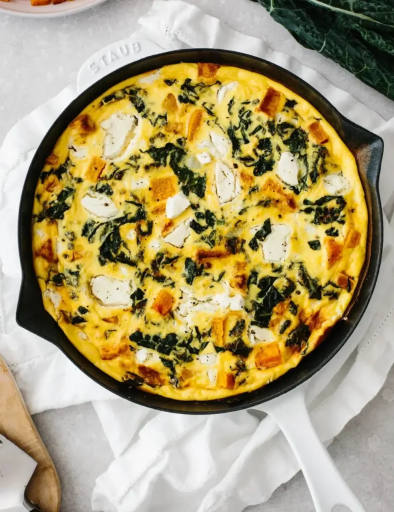 Kale and butternut squash frittata in a white pan, with goat cheese on top