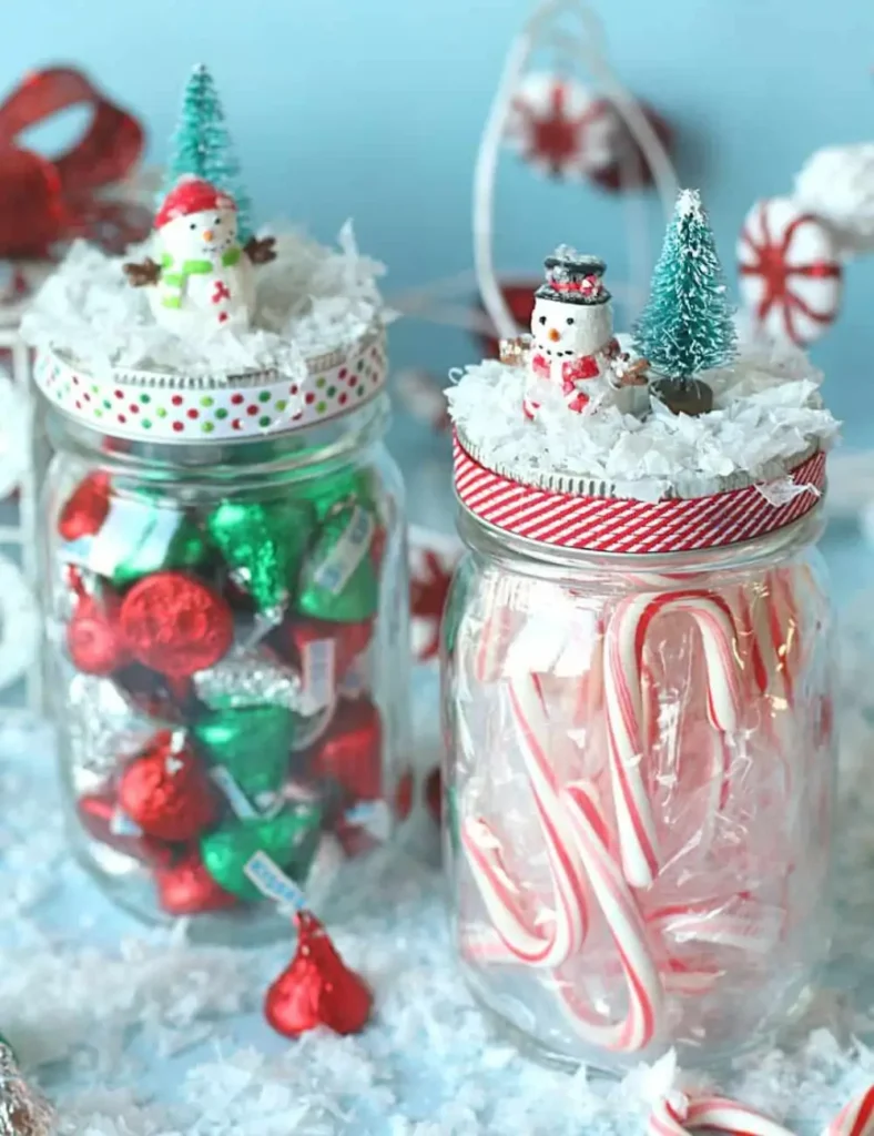 Mason jars filled with Christmas candy, with snow-covered lids topped with miniature snowmen and bottlebrush trees and tied with ribbon.