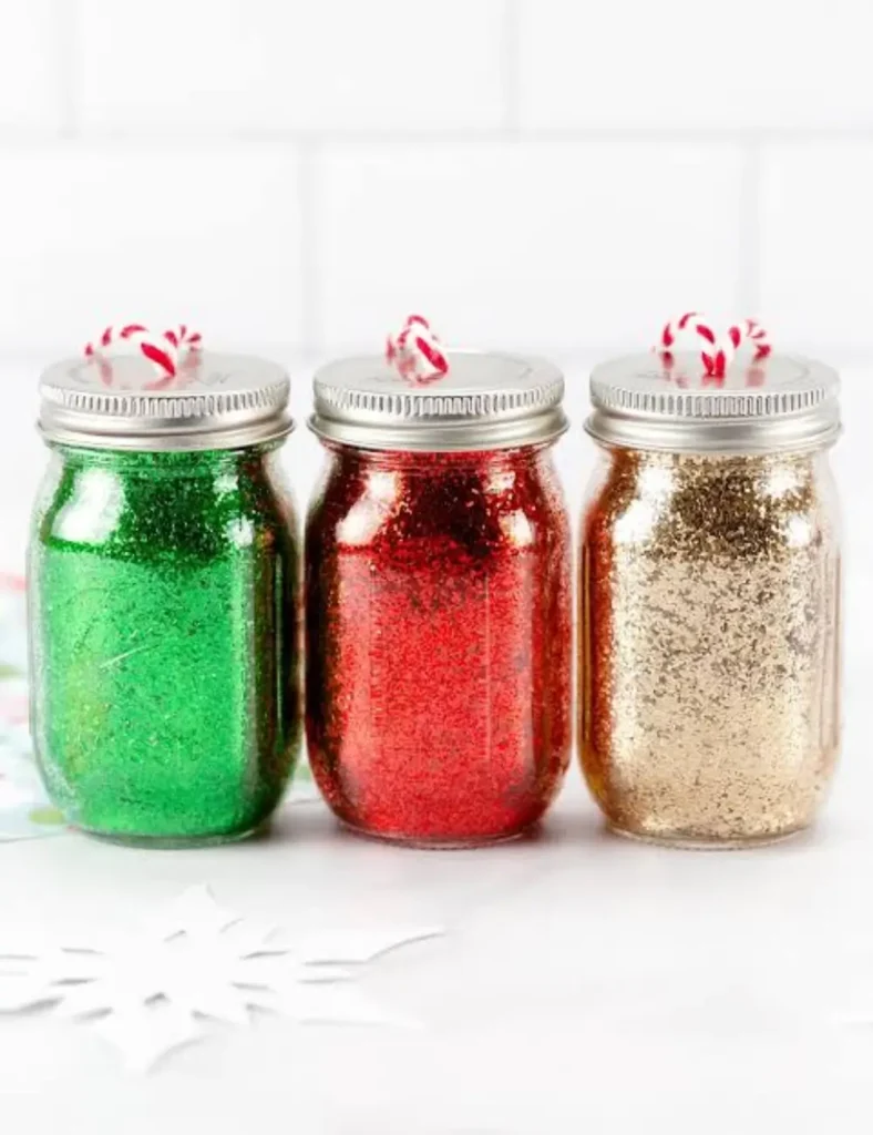 Mini mason jar ornaments coated in colorful glitter, hanging from a Christmas tree on ornament string.