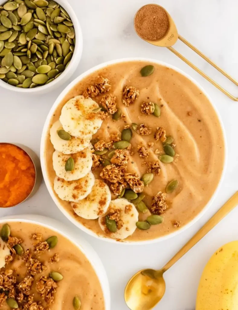 Orange pumpkin smoothie bowl topped with granola, pumpkin seeds and a dusting of cinnamon