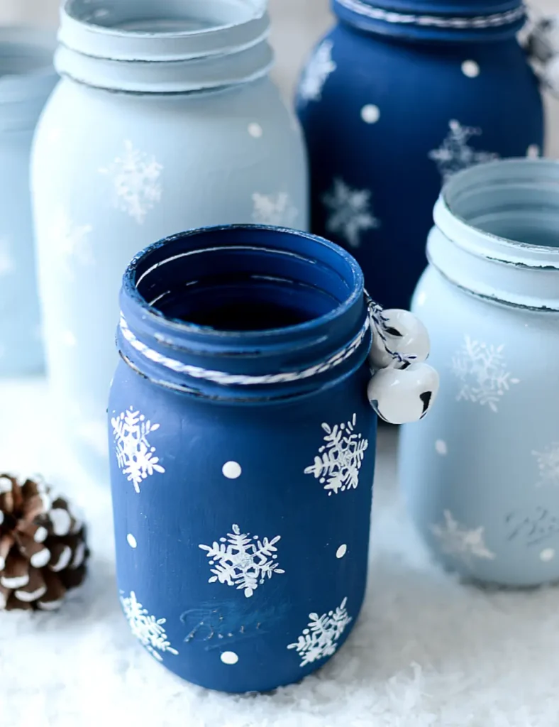Painted mason jar decorated with white stamped snowflakes and dotted details, with a bell tied around the neck.