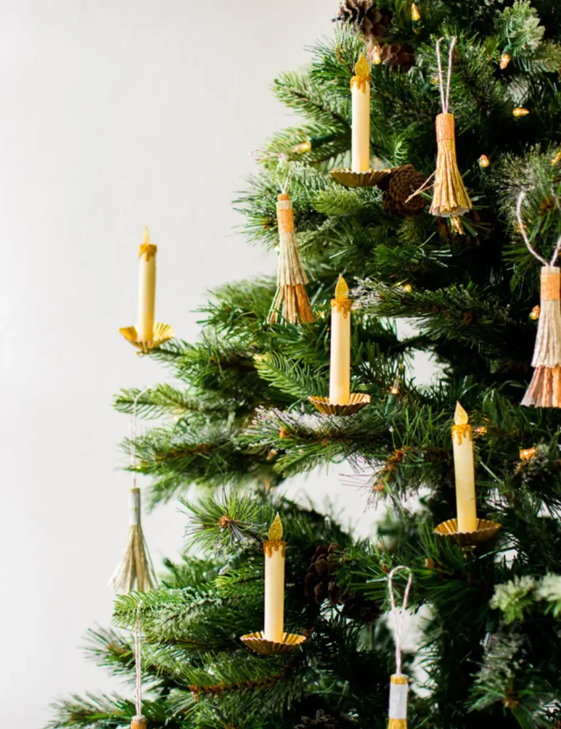 Paper candle ornaments with gold foil bases and glittered flames clipped onto Christmas tree branches.
