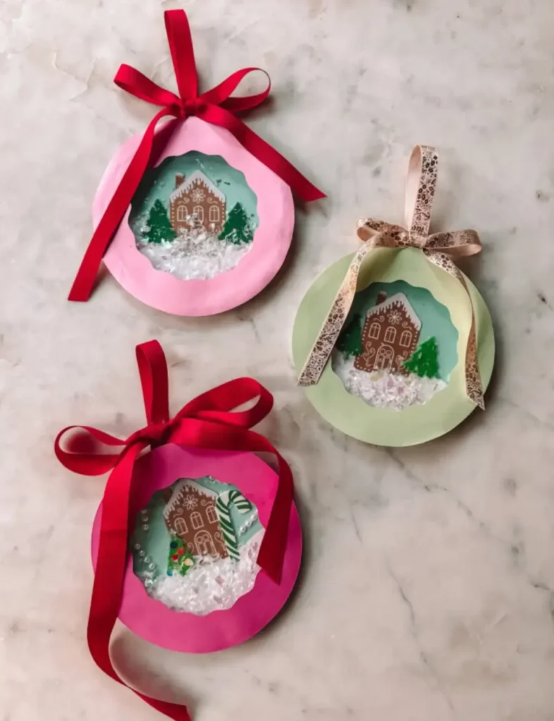 Paper plate snow globes with cardstock scenes, felt trees and iridescent confetti snow behind cellophane.