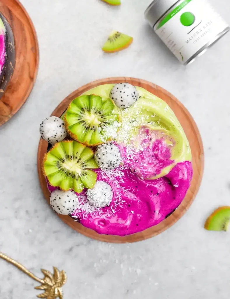 Pink and green dragon fruit matcha smoothie bowl topped with kiwi, pitaya, and coconut