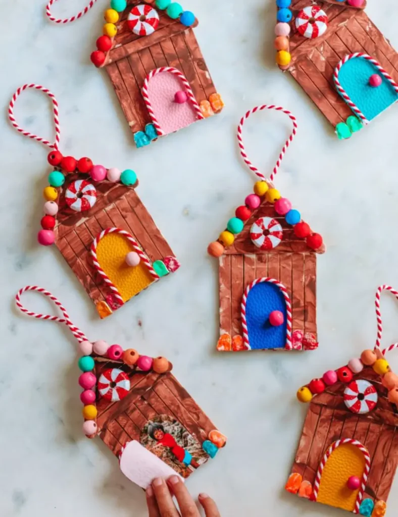 Popsicle stick gingerbread house ornaments decorated with painted wooden bead candy and a small fabric door.