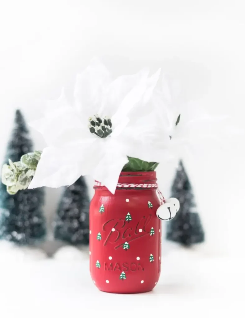 Red painted mason jar covered in hand-painted green Christmas trees with brown trunks and white snowy tips.