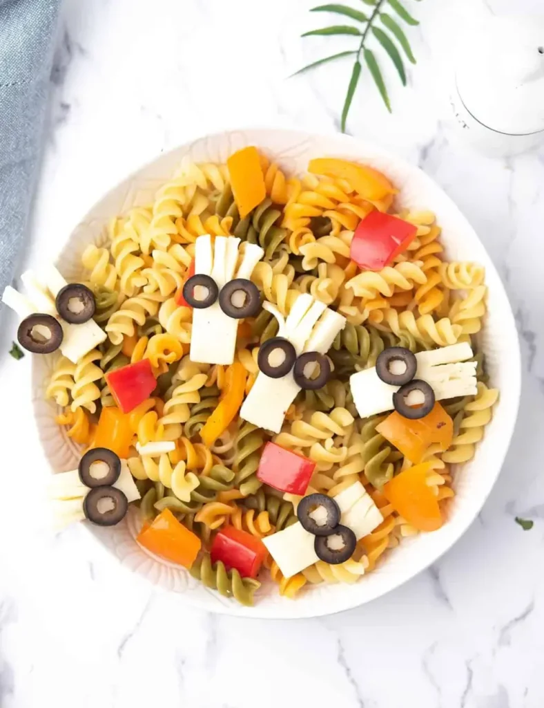 Rotini pasta salad with bell peppers and tomatoes topped with string cheese monster heads with olive eyes