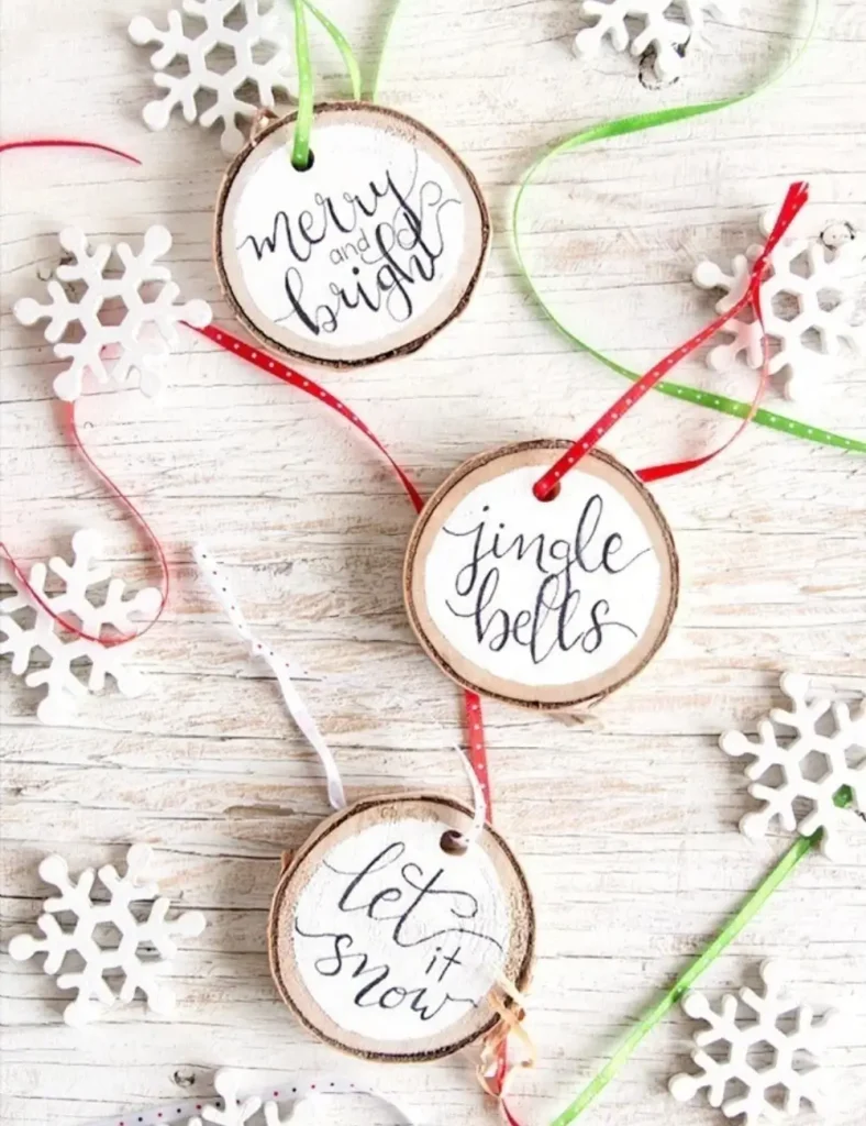 Round wood slice ornaments with white painted centers and black hand-lettered text, hung on thin ribbon.