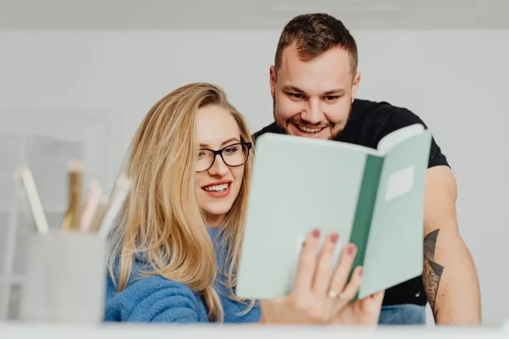 Smiling couple enjoying a book together in a cozy, bright home setting. Fun Date Night at Home Ideas