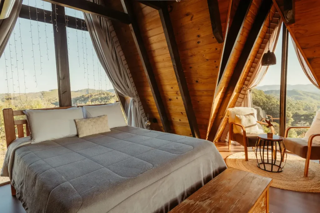 Spacious wooden A-frame bedroom featuring a large bed, cozy chairs, and a stunning mountain view.