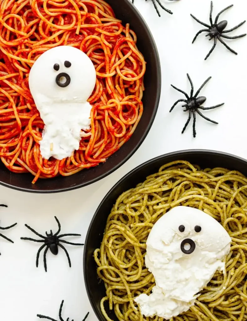 Spaghetti in tomato sauce on a black plate topped with a burrata ghost with an olive face