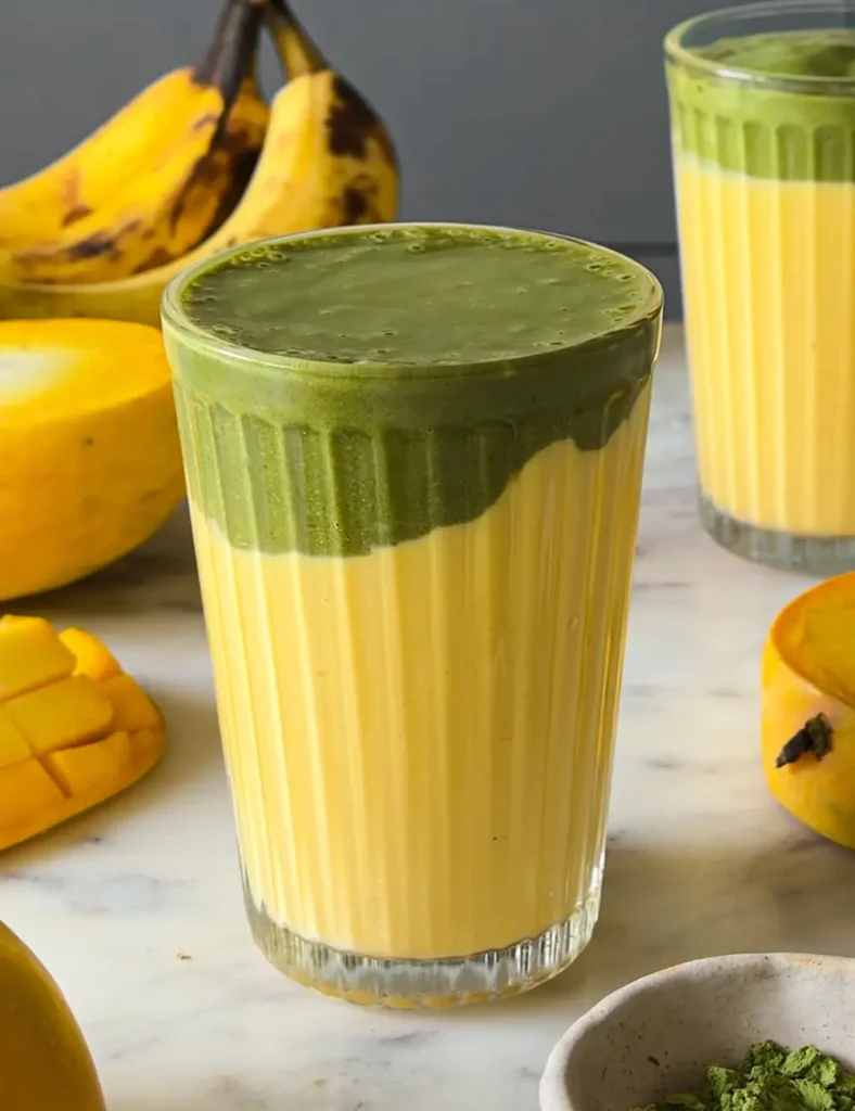 Tall glass of two-tone mango matcha smoothie with a golden mango layer under a green matcha layer
