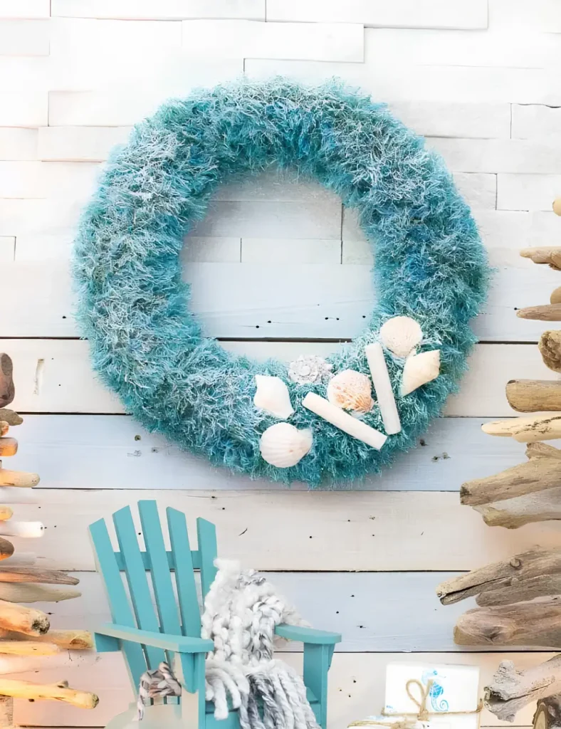 Teal upcycled wreath wrapped in knitted fabric with a cluster of seashells and light snow spray