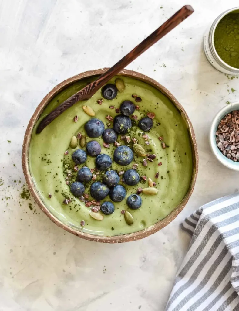Thick green matcha smoothie bowl topped with blueberries, cacao nibs, and pumpkin seeds