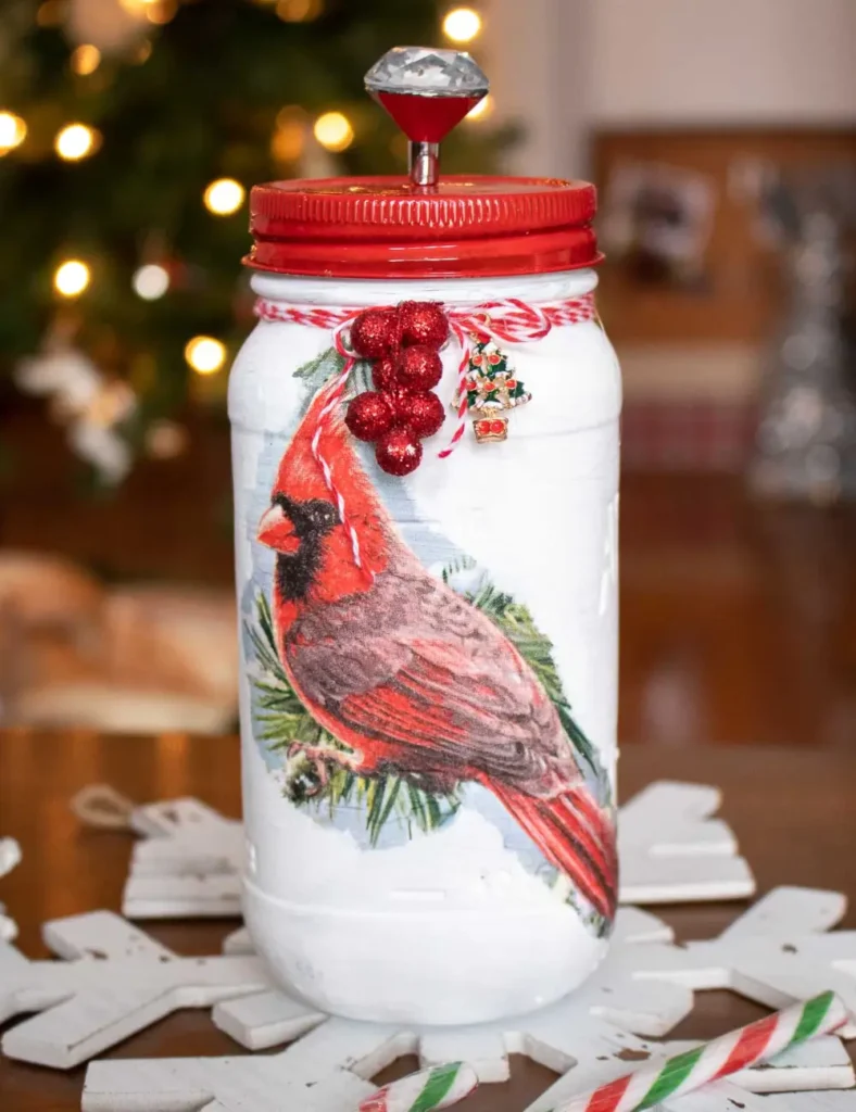White painted mason jars decorated with a cardinal napkin decoupage, red lids with decorative knobs and twine around the necks.