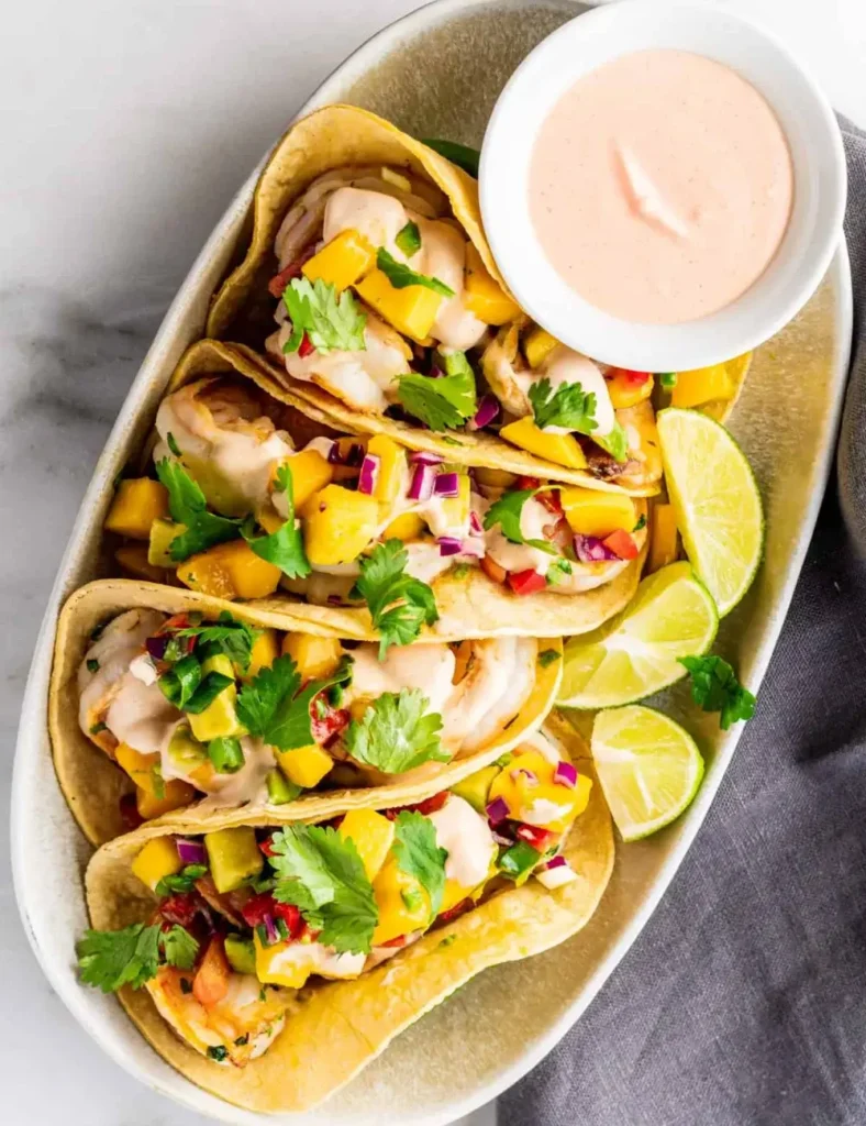 Shrimp tacos topped with mango salsa and chipotle crema on an oval platter