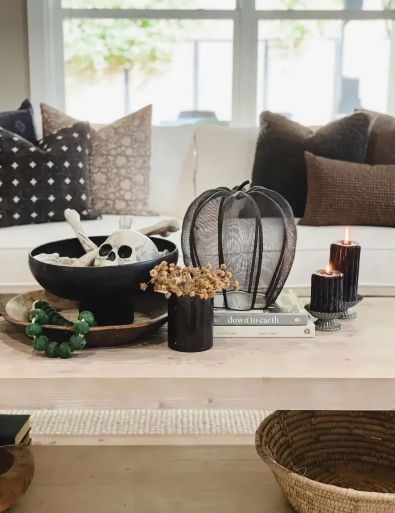 Black bowl filled with skeleton bones styled with a mesh pumpkin, dried florals and dark taper candles on a coffee table