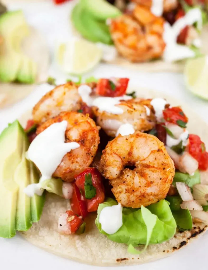 Sheet pan shrimp tacos topped with pico de gallo and lime crema on corn tortillas