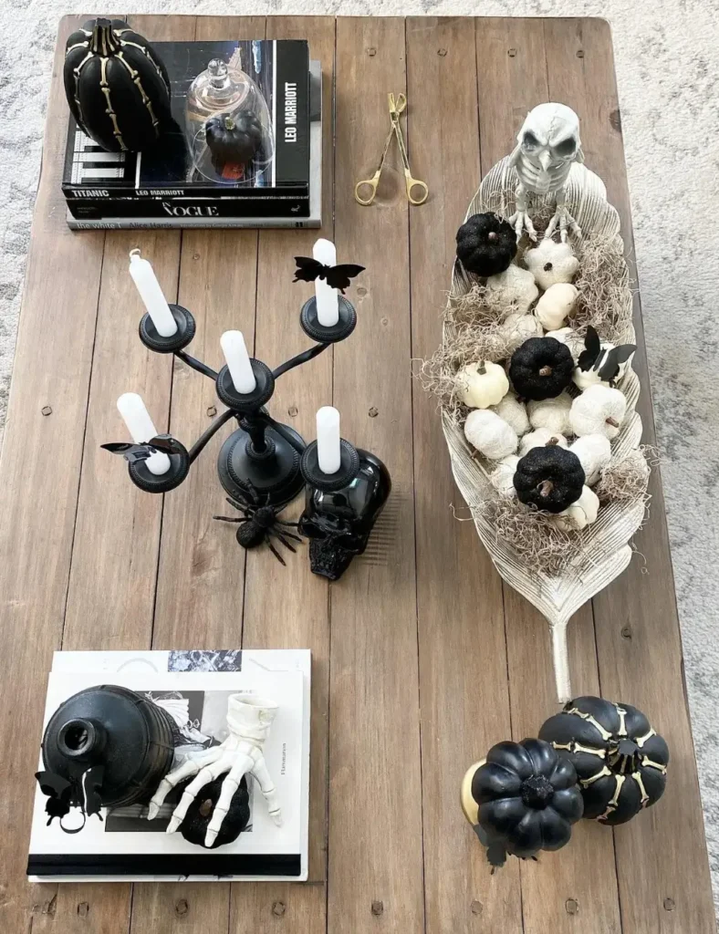 Overhead view of gothic Halloween coffee table decor with a black candelabra, skeleton hand, black pumpkins and a feather-shaped bowl of mini pumpkins