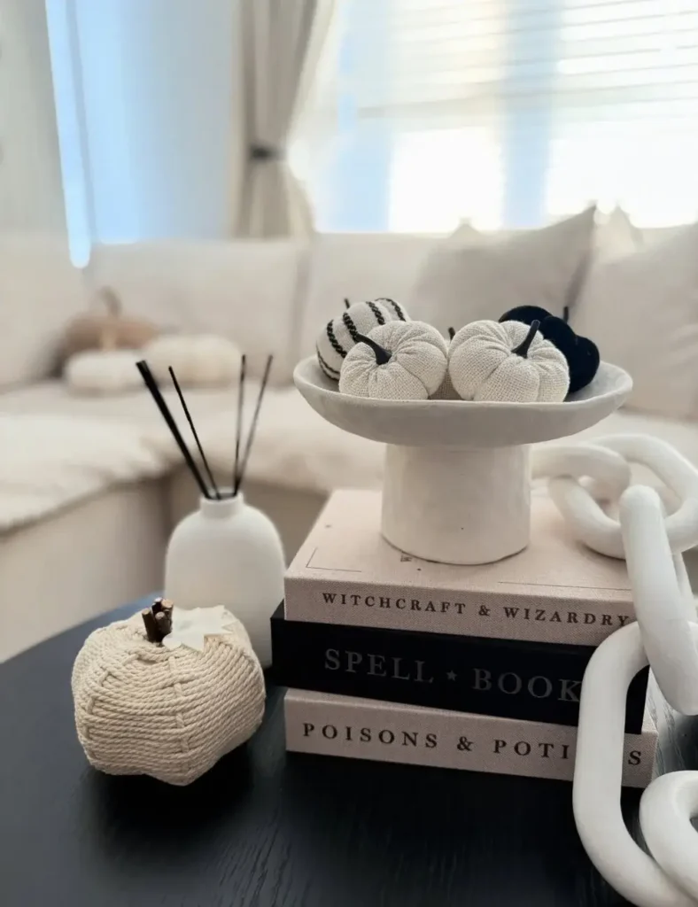Neutral Halloween coffee table styling with fabric pumpkins in a pedestal bowl, a woven rope pumpkin and a stack of spellbook-themed decor books