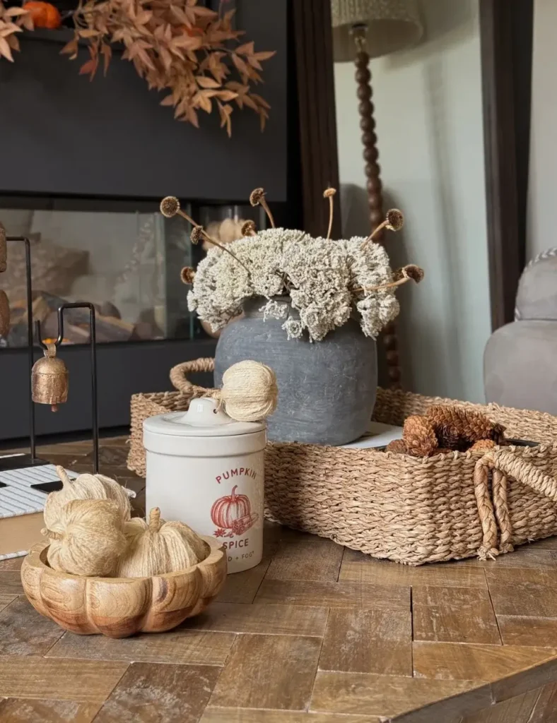 Neutral coffee table styling with a pumpkin spice crock, woven yarn pumpkins in a wood bowl and dried florals in a stone vase
