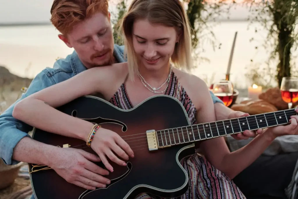 A couple enjoying a romantic sunset picnic by the lake while playing guitar together