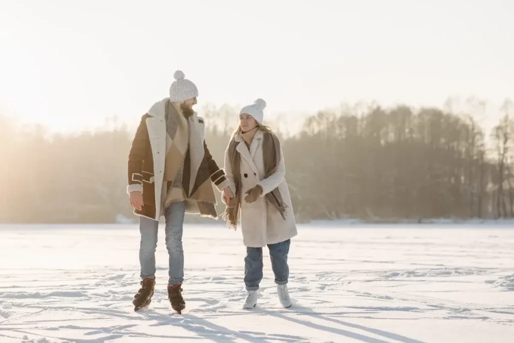 A couple holding hands while ice skating on a snowy outdoor landscape during winter
