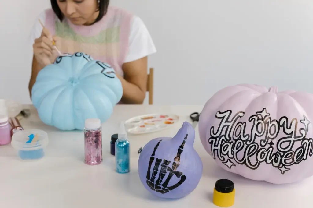 A person painting pastel Halloween pumpkins with designs and text at a crafting table