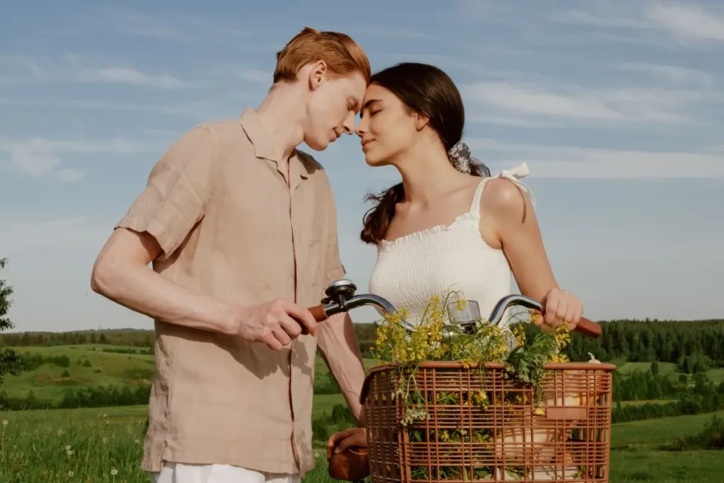 A young couple shares a tender moment with a vintage bicycle in a lush summer landscape