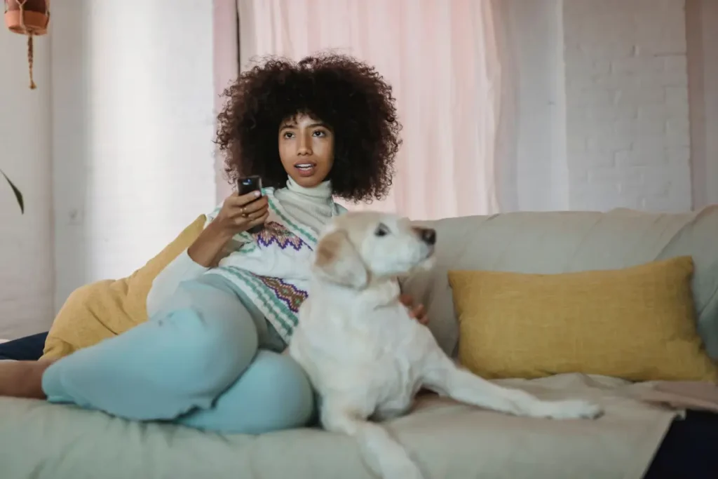 A young woman with curly hair enjoys a cozy moment with her dog on a living room couch