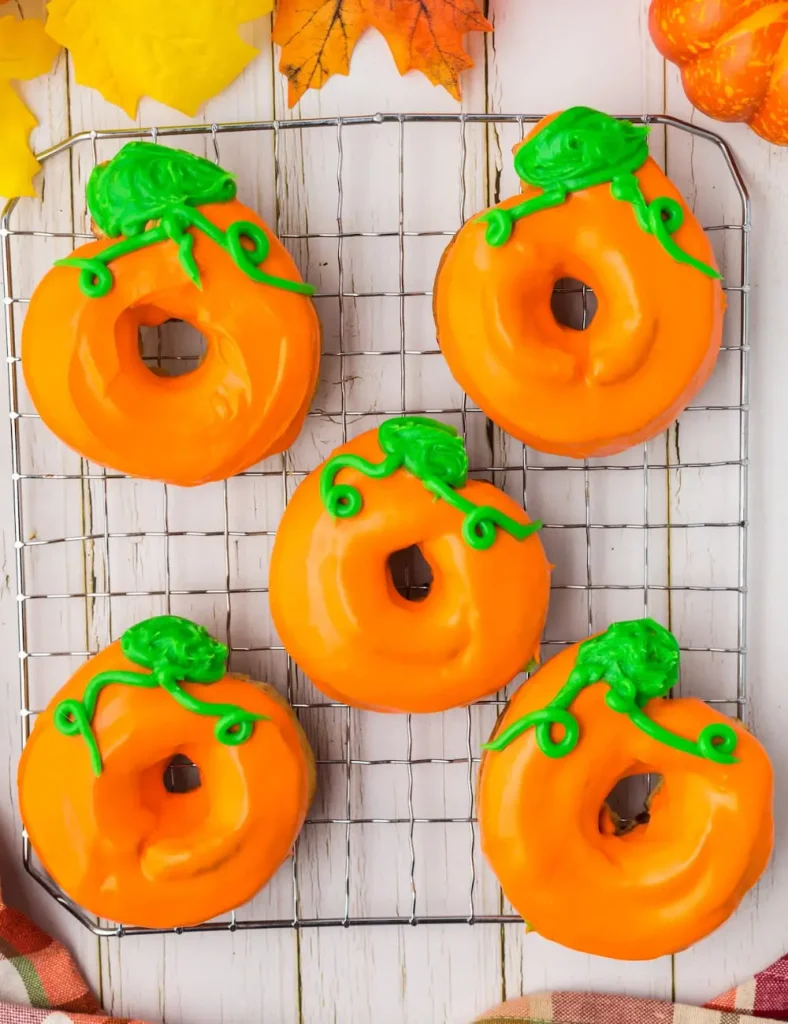 Air fryer donuts glazed orange with green icing shaped like pumpkin stems