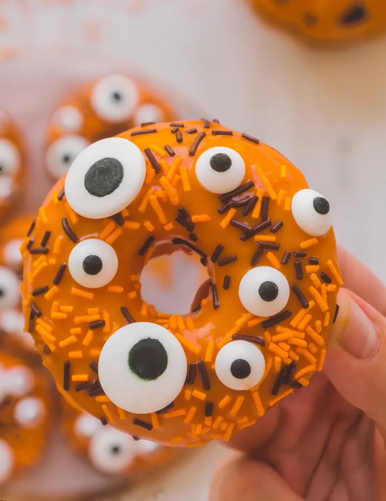 Baked orange glazed monster donuts topped with candy eyeballs and Halloween sprinkles