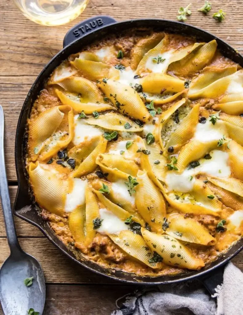 Baked pumpkin and pesto stuffed pasta shells in a skillet topped with melted mozzarella and fresh basil