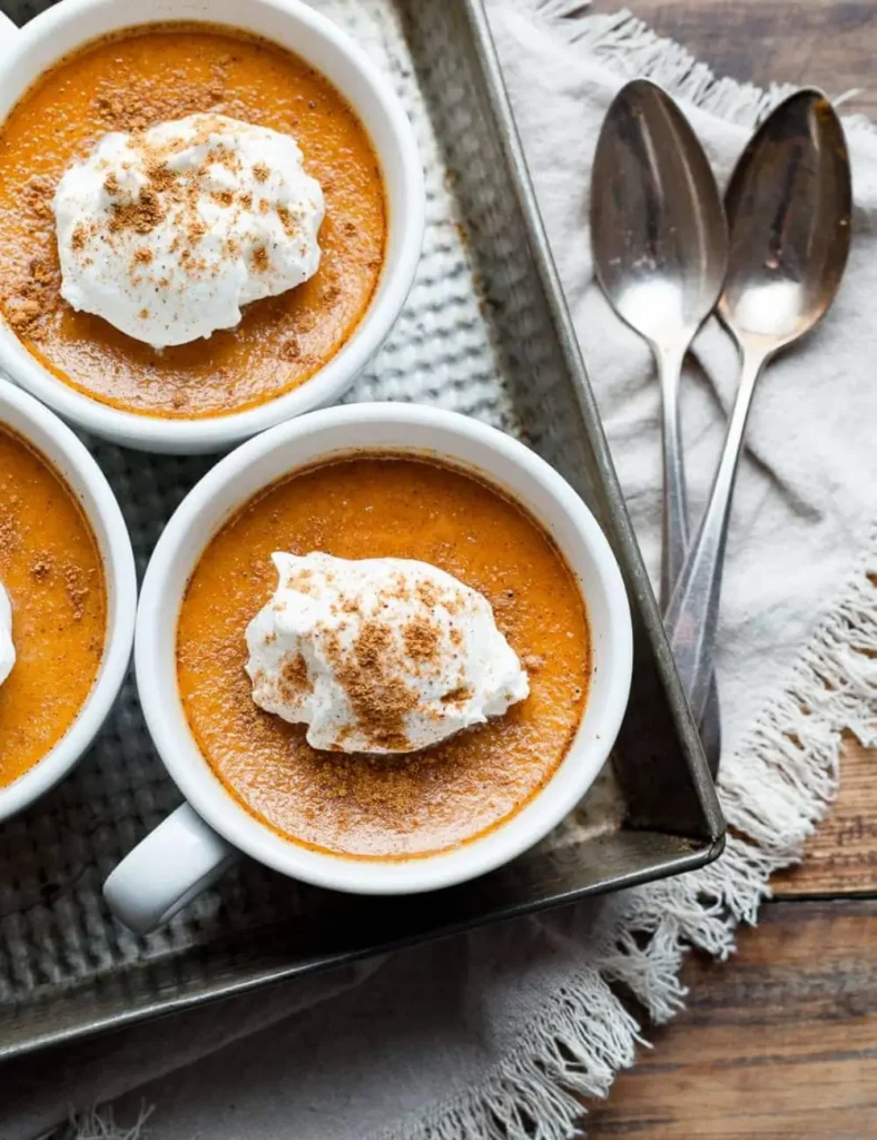 Baked pumpkin custard in small ramekins topped with whipped cream and pumpkin spice