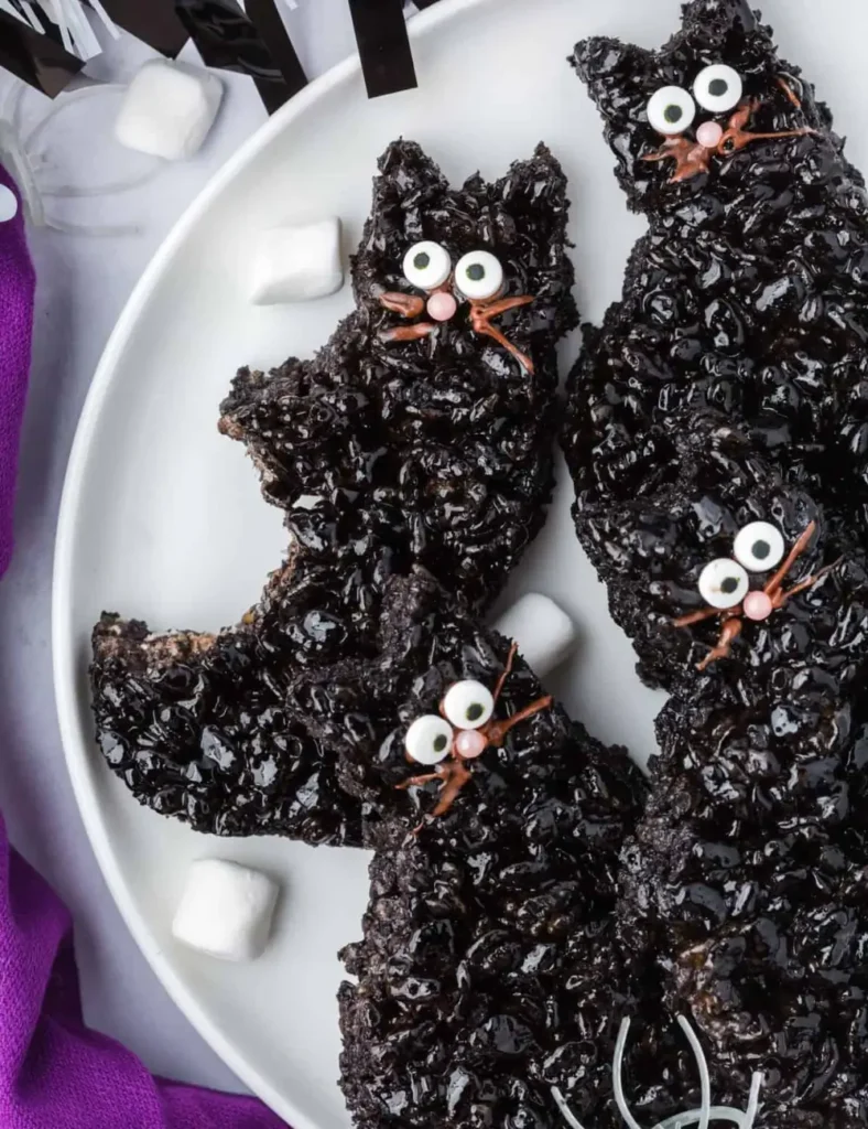 Black cat-shaped Rice Krispie treats with candy eyes and a pink nose