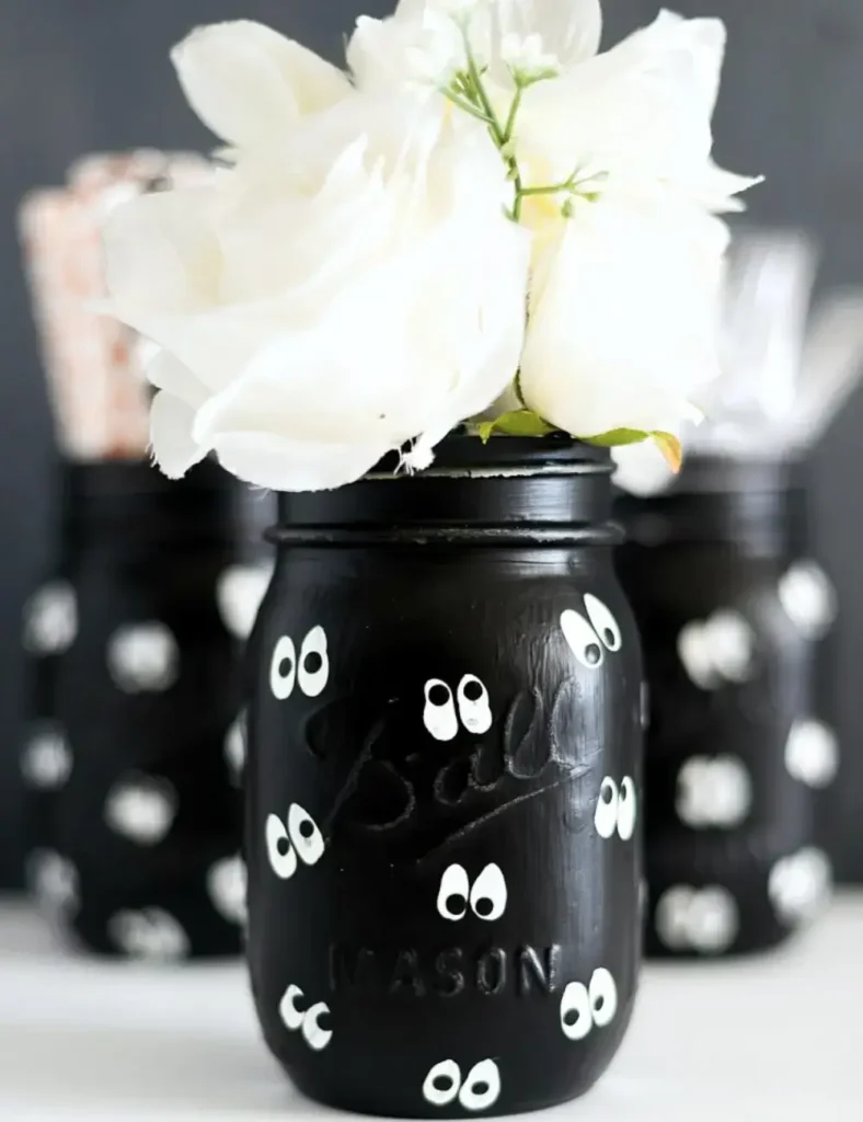 Black mason jars hand-painted with whimsical googly-eye designs for Halloween decor