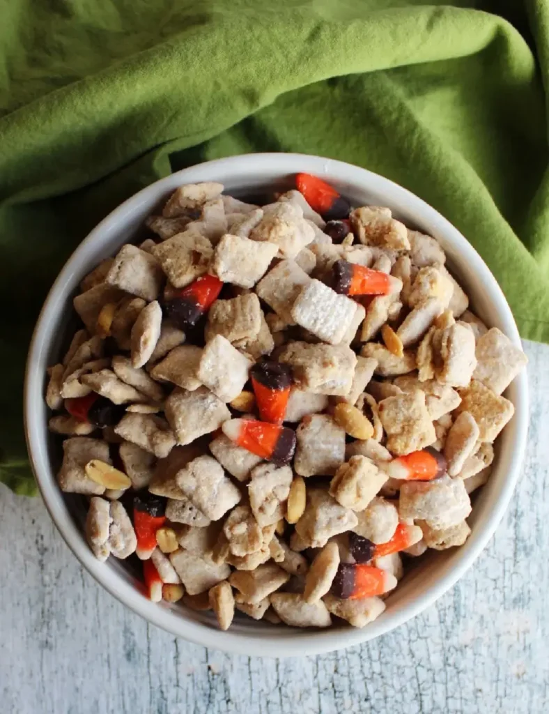 Bowl of fall puppy chow mix with white chocolate coated cereal, candy corn, and peanuts