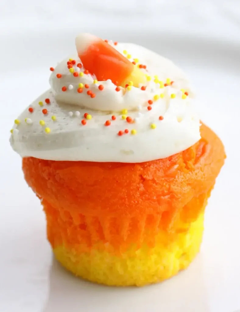 Candy corn cupcake with yellow and orange cake layers, white frosting, sprinkles and a candy corn topping