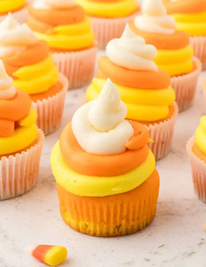 Candy corn cupcakes with yellow, orange and white frosting arranged on a worktop