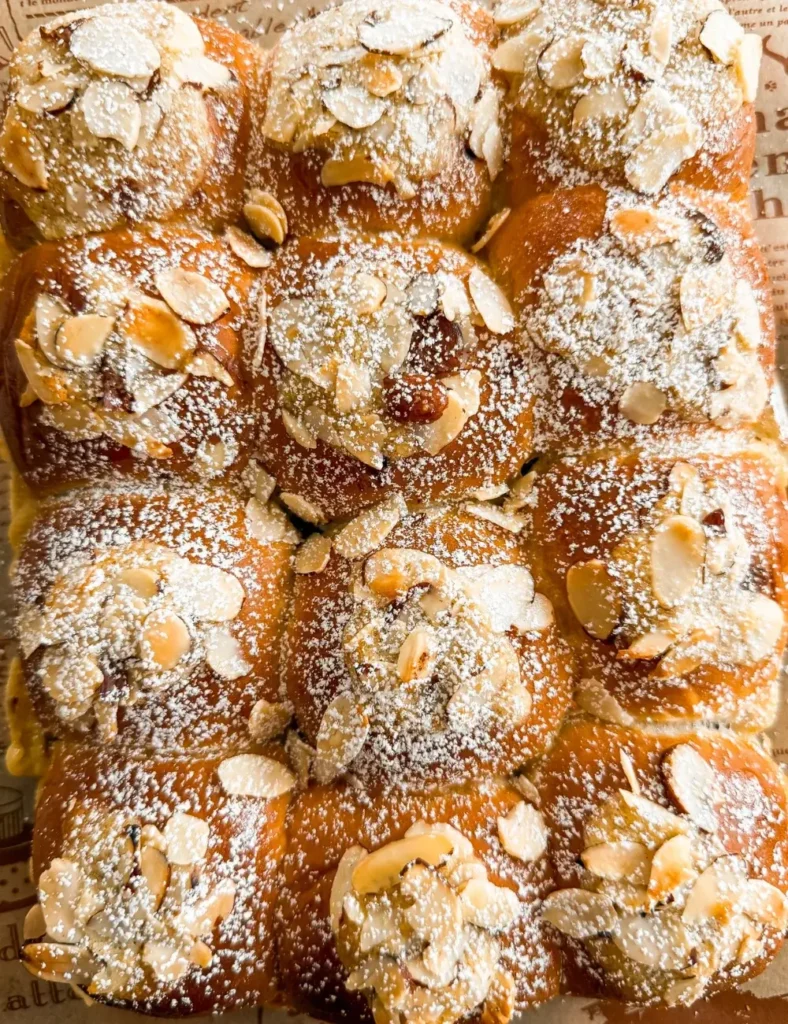 Chocolate almond croissants topped with sliced almonds and powdered sugar on a baking tray