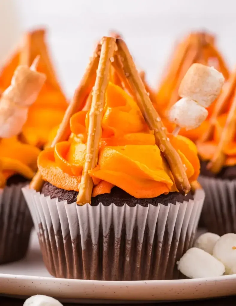 Chocolate cupcakes decorated with orange and yellow flame frosting, pretzel logs, and marshmallows