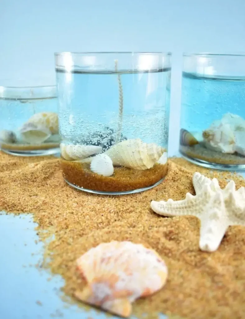 Clear gel wax candle with sand and seashells layered inside, resembling an ocean floor