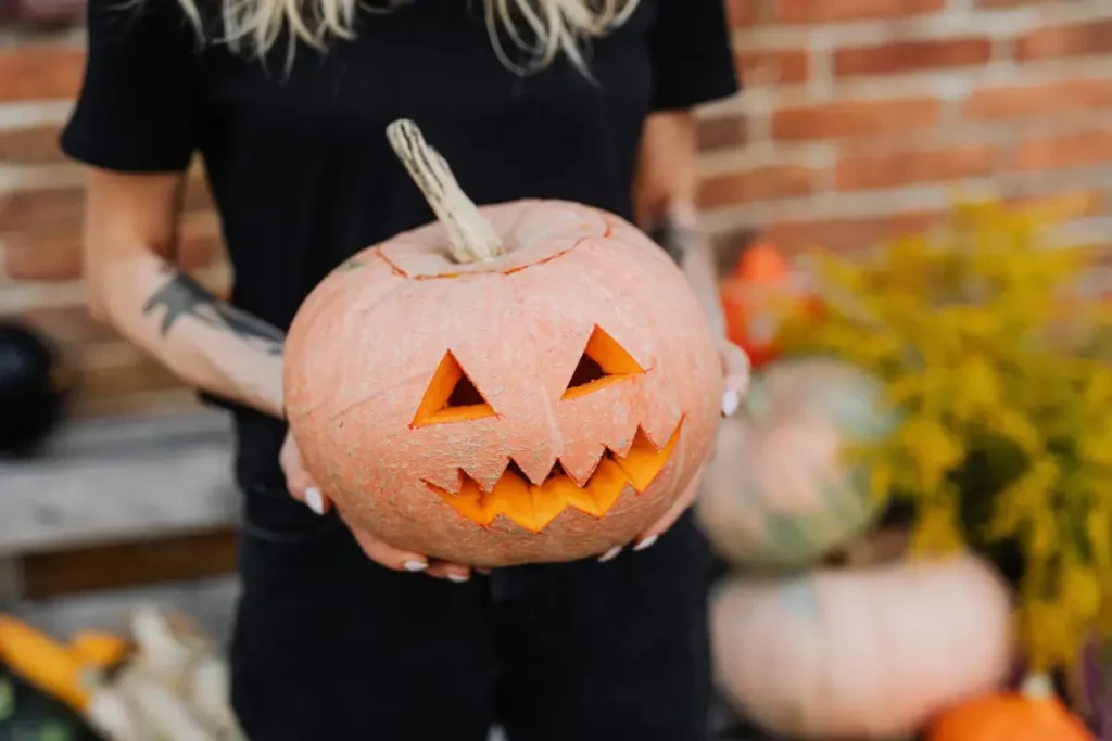 Close-up of a woman holding a carved jack-o'-lantern pumpkin outdoors, embracing Halloween spirit