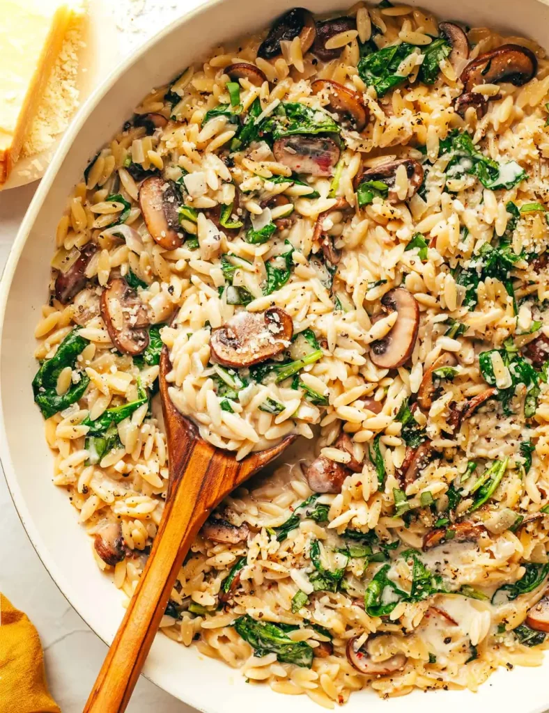 Creamy garlic mushroom orzo in a skillet with browned mushrooms, spinach and grated Parmesan