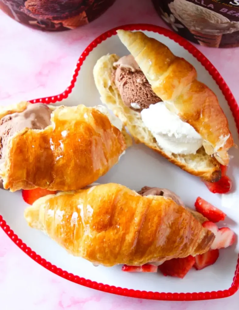 Croissant ice cream sandwich with a glossy candy shell top and scoops of ice cream, served with strawberries