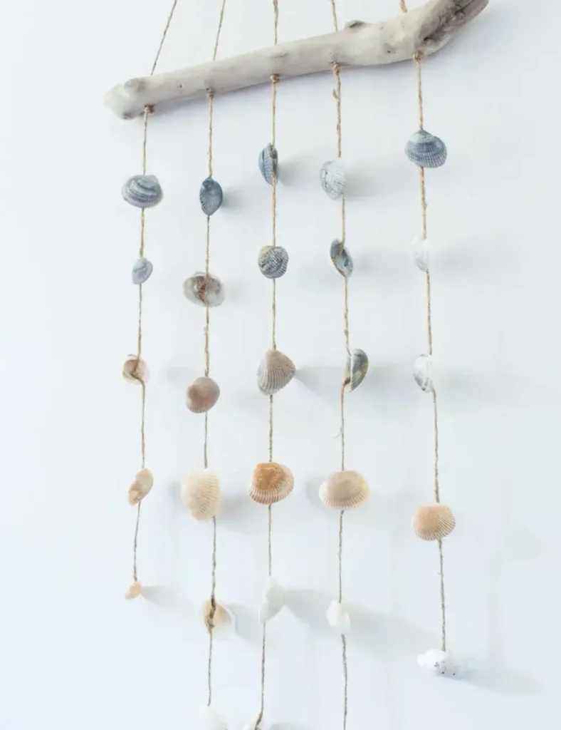 Driftwood wind chime with hanging seashells against a coastal-style wall