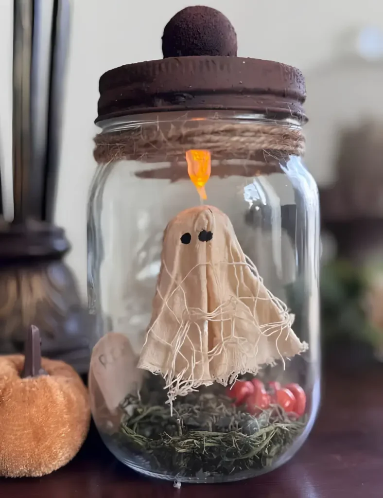 Floating ghost mason jar craft with a muslin ghost, mini gravestone and pumpkin, lit by a tea light