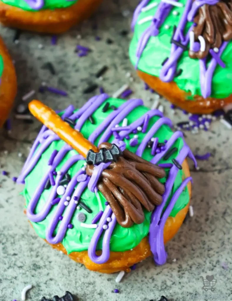 Fried biscuit donut decorated with green frosting and a pretzel stick witch broom
