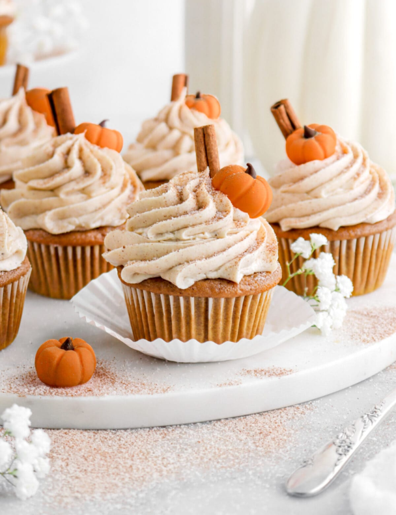 Frosted pumpkin cupcakes topped with cinnamon sticks and fondant pumpkin decorations