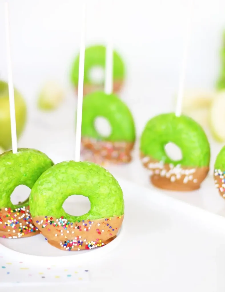 Green apple-colored donuts on sticks dipped in caramel and sprinkles